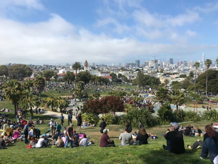 A group of people are sitting on top of a grassy hill in a park.