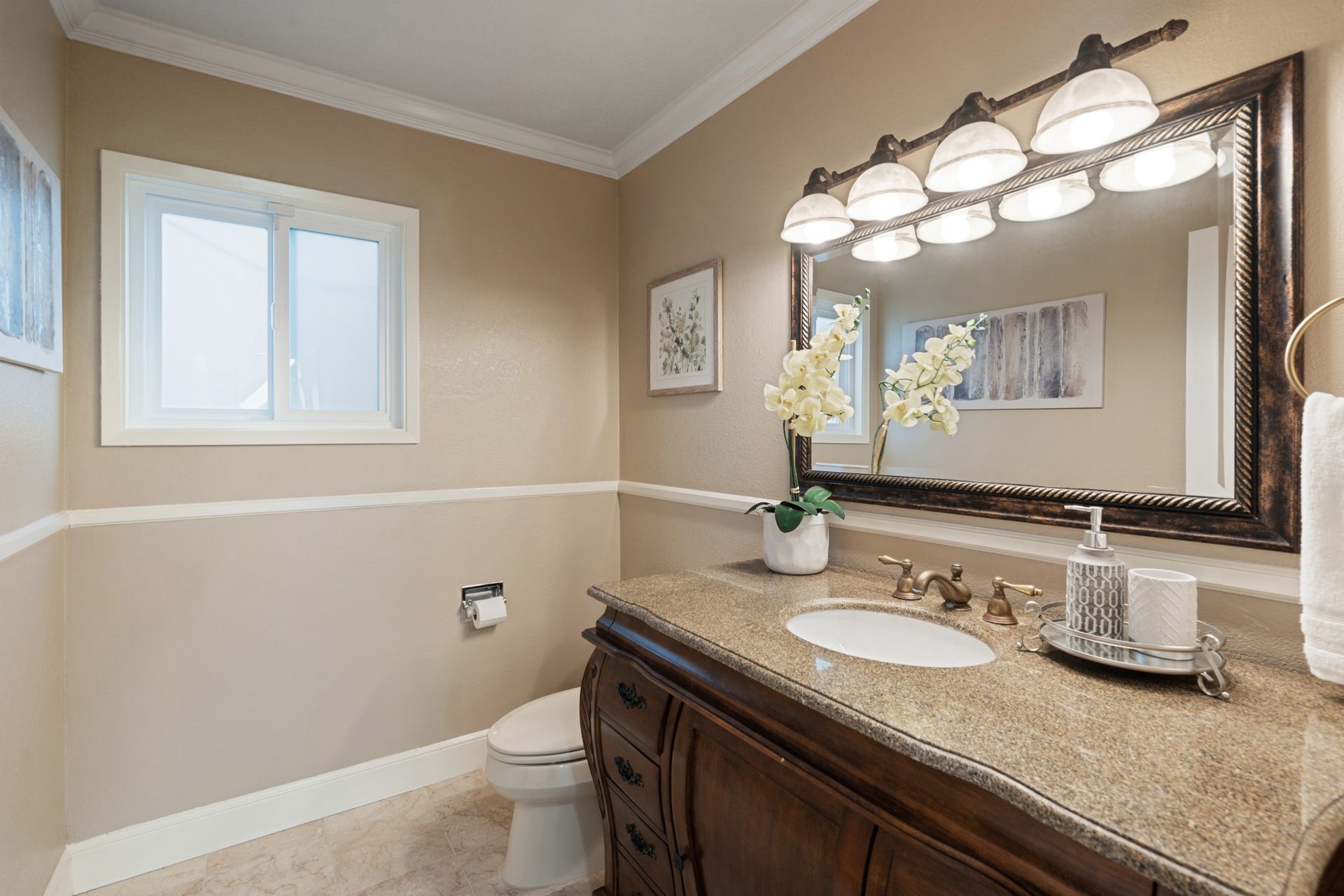 A bathroom with a sink , toilet , mirror and window.