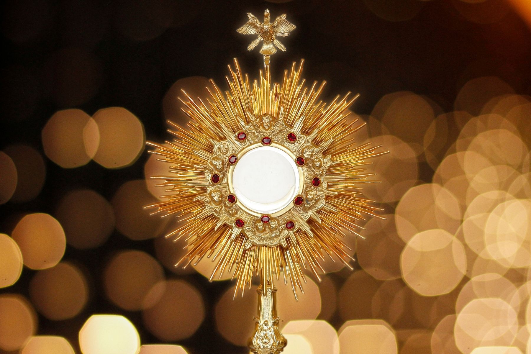Monstrance displaying consecrated Eucharist on an altar, flanked by lit candles.