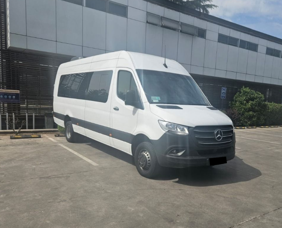 Una furgoneta de pasajeros Mercedes-Benz Sprinter blanca estacionada en un aparcamiento pavimentado