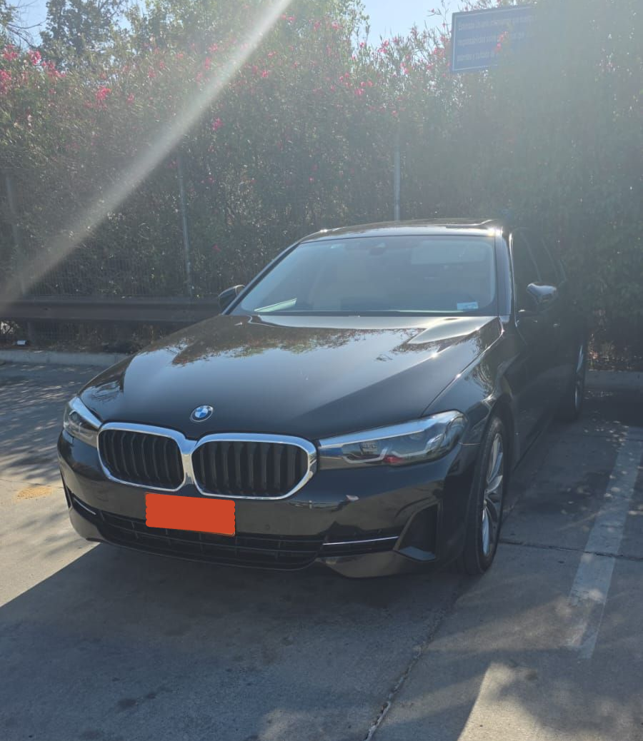 Un sedán BMW de color oscuro estacionado en una zona soleada al aire libre con árboles al fondo.