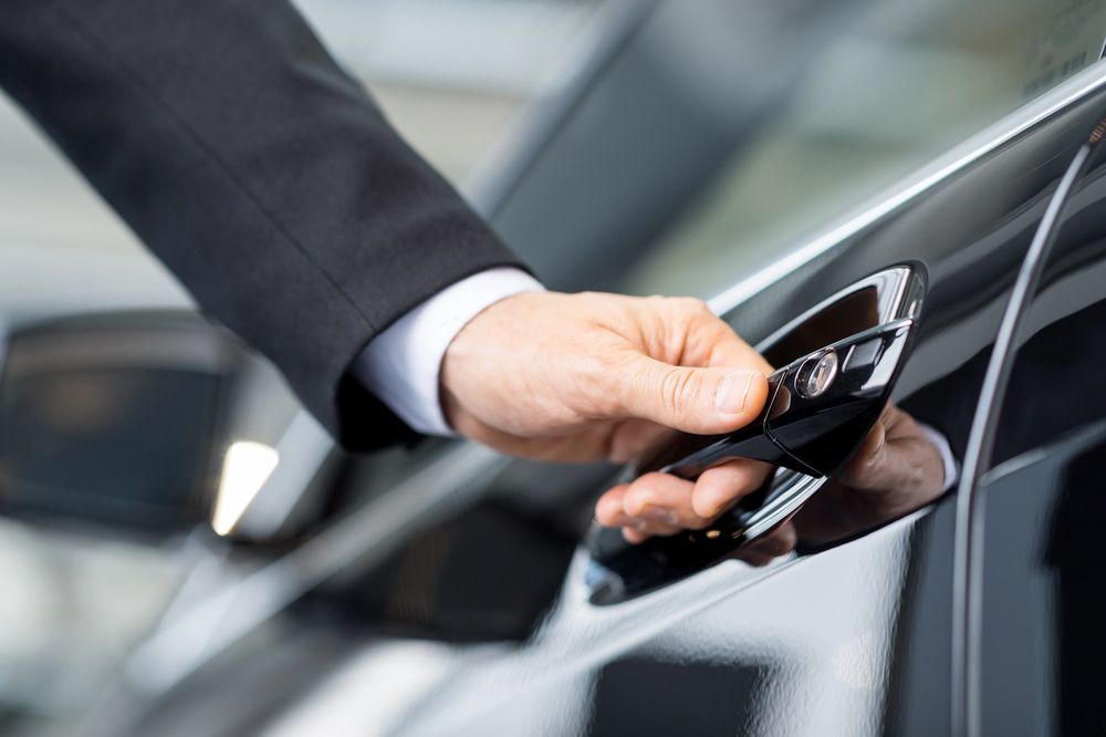 Mano con traje negro abriendo la puerta de un coche.