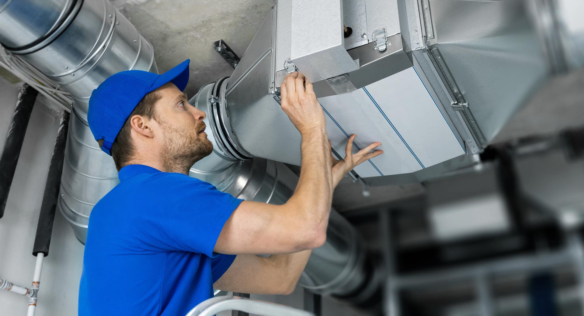 HVAC technician in blue uniform installing an air filter in ductwork; indoor setting.