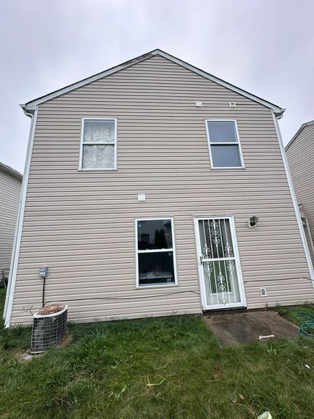 Back of a two-story beige house with windows, a white door, and a grassy yard