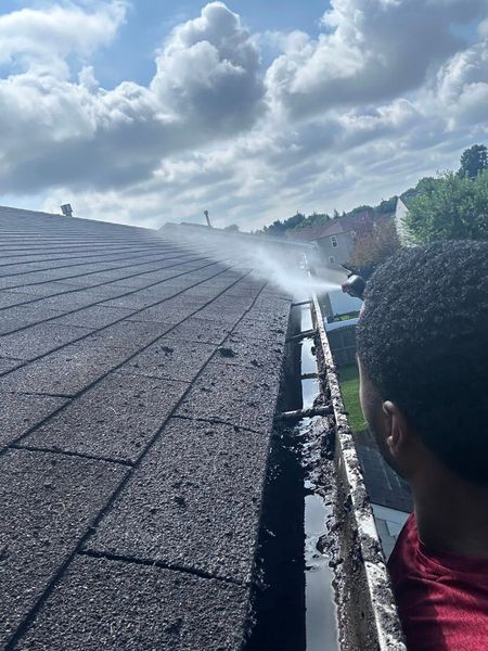 Person spraying water onto a dark roof from the edge under a cloudy sky