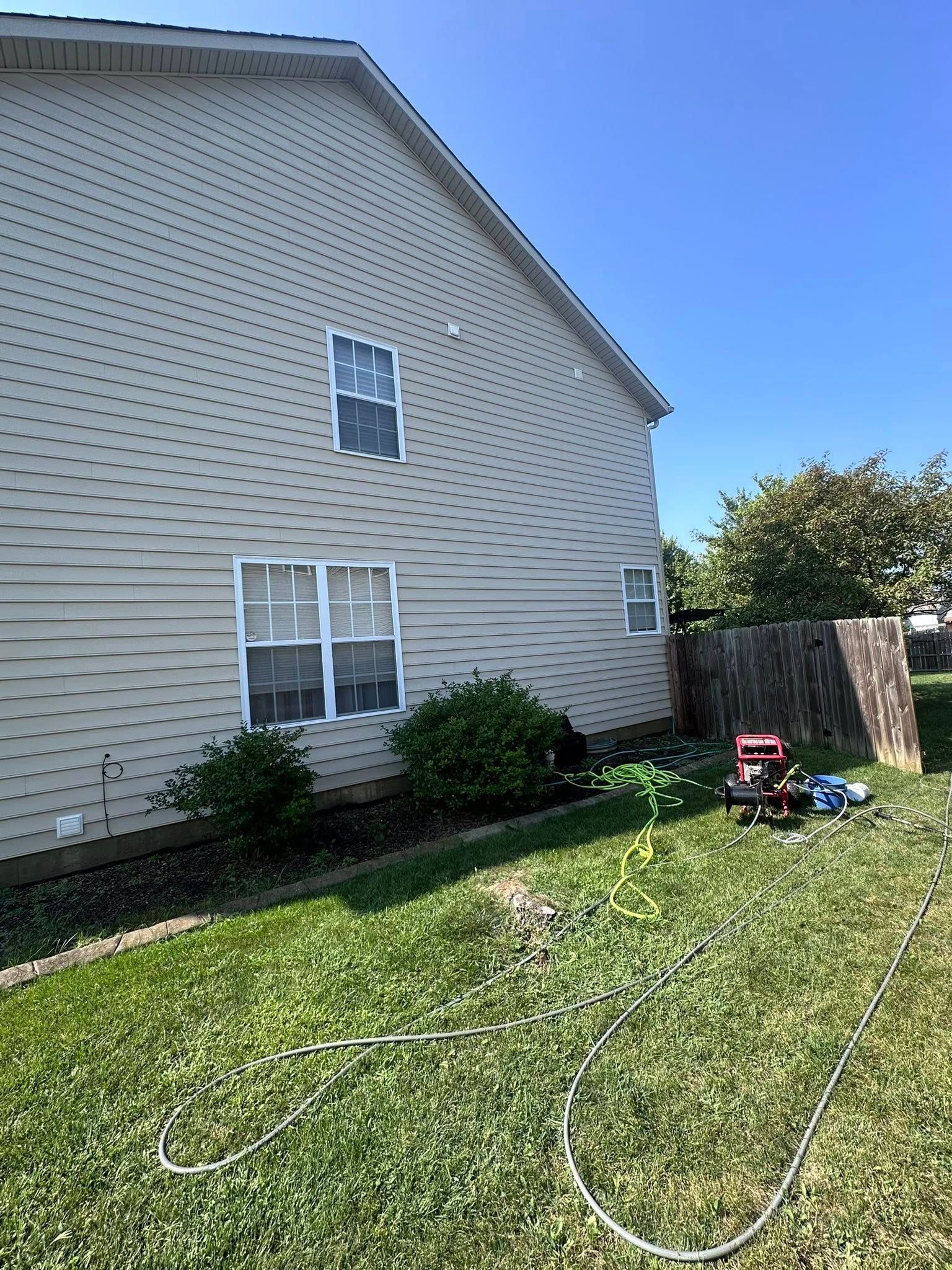 Backyard beside a beige house with lawn, garden hose, and a red lawn mower near a fence.