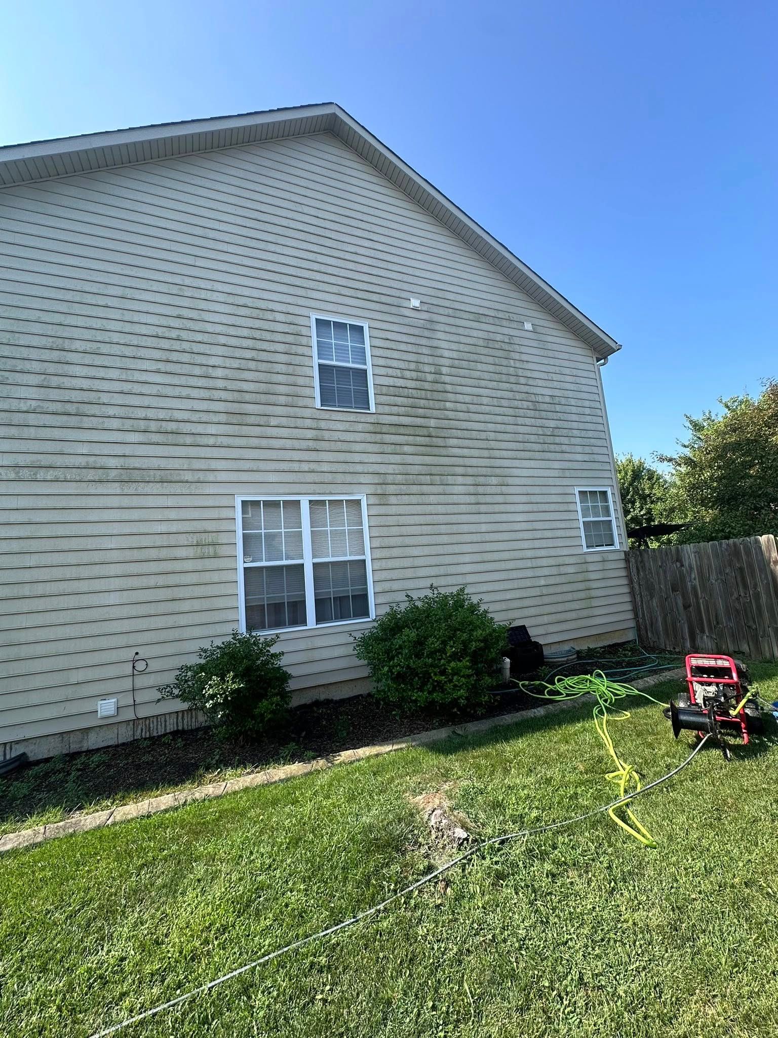 Side view of beige house with white-trim windows, green lawn, bushes, and a red mower near a fence.