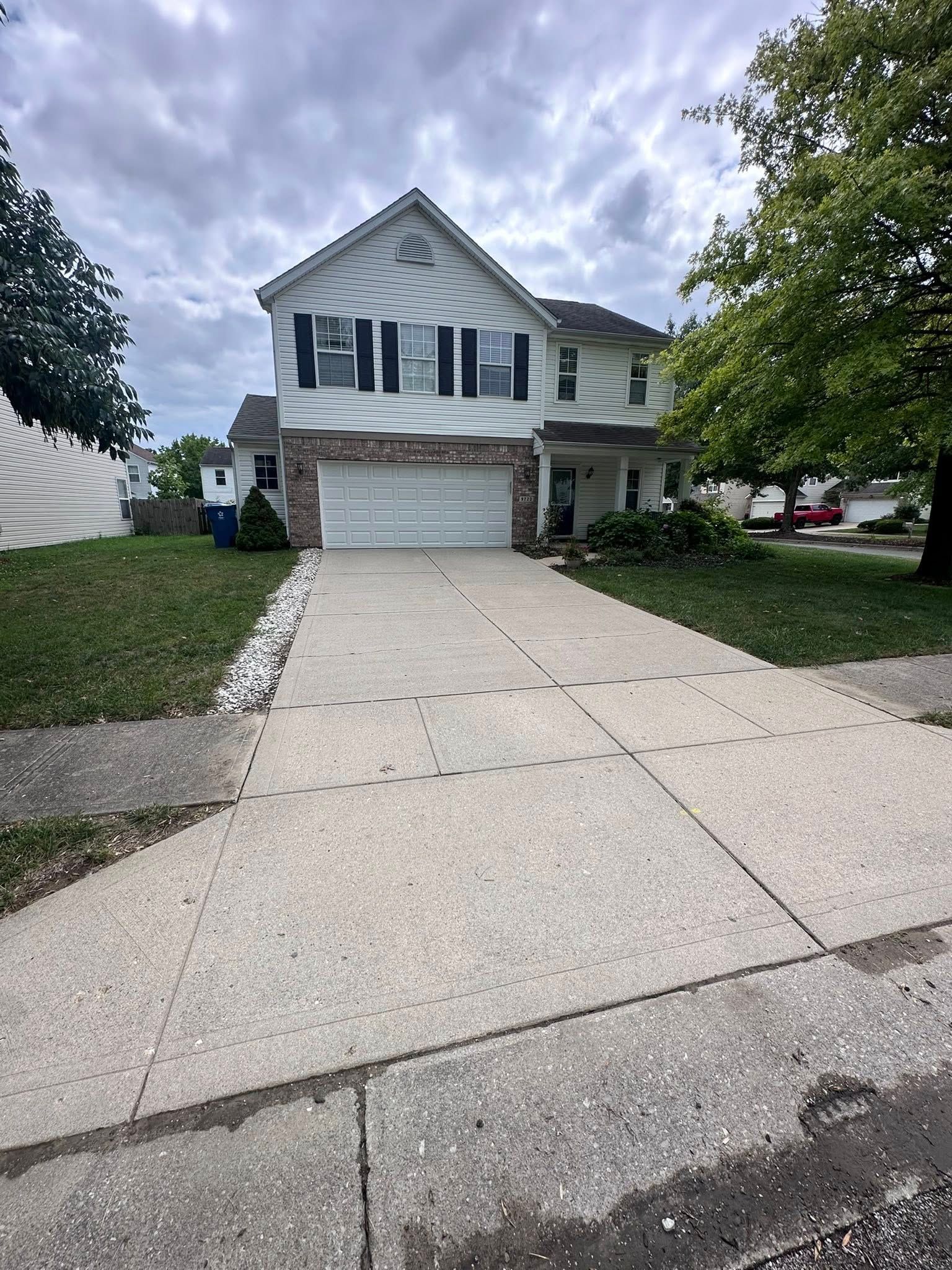 Suburban two-story house with white siding, double garage, and long concrete driveway under cloudy sky