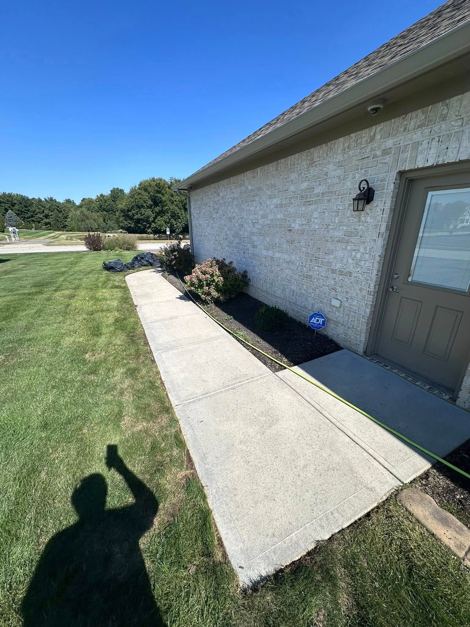 Concrete walkway beside a stucco house and green lawn, with a person’s shadow in the foreground.