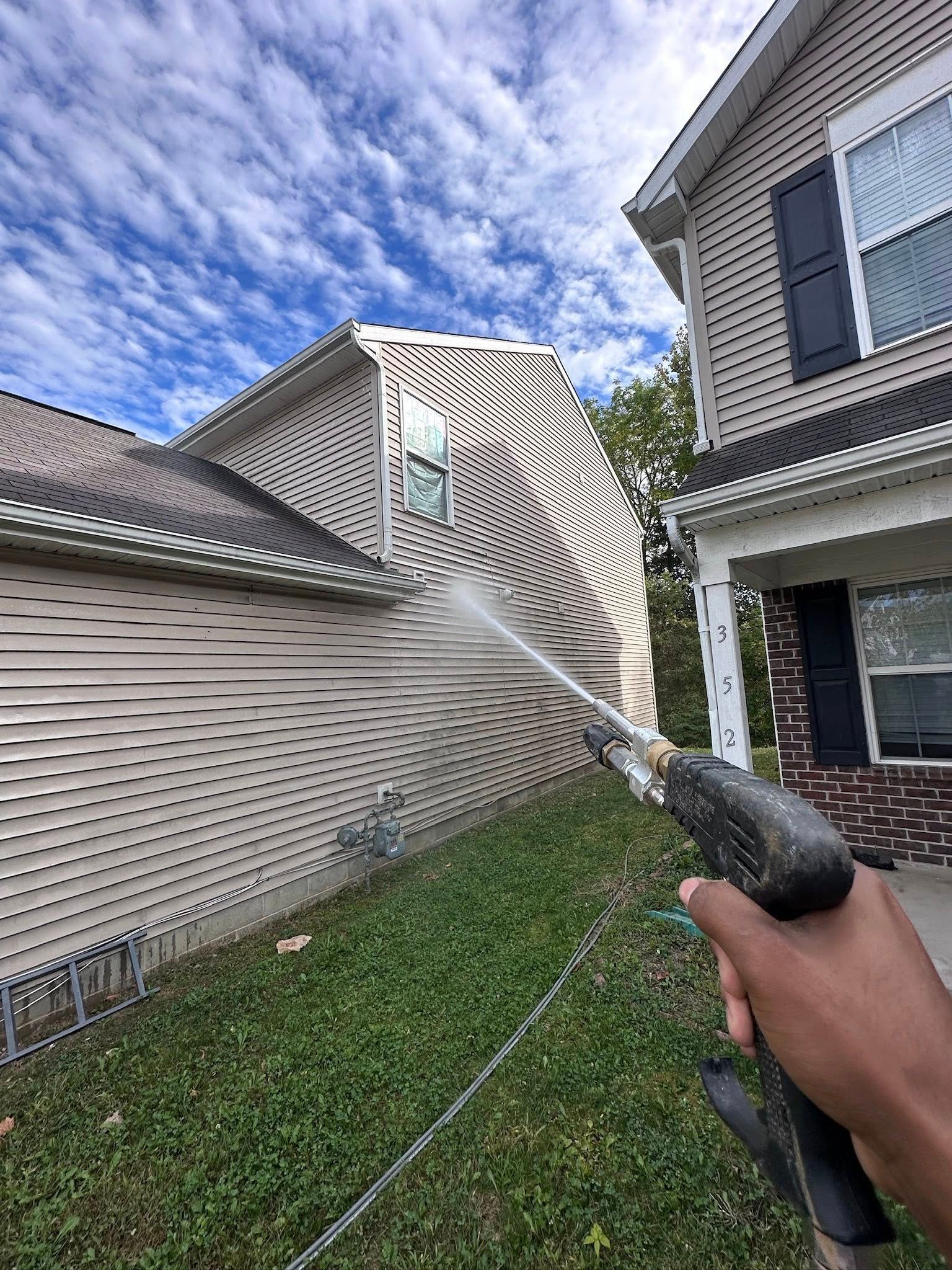 Person spraying a townhouse wall with a pressure washer in a suburban yard