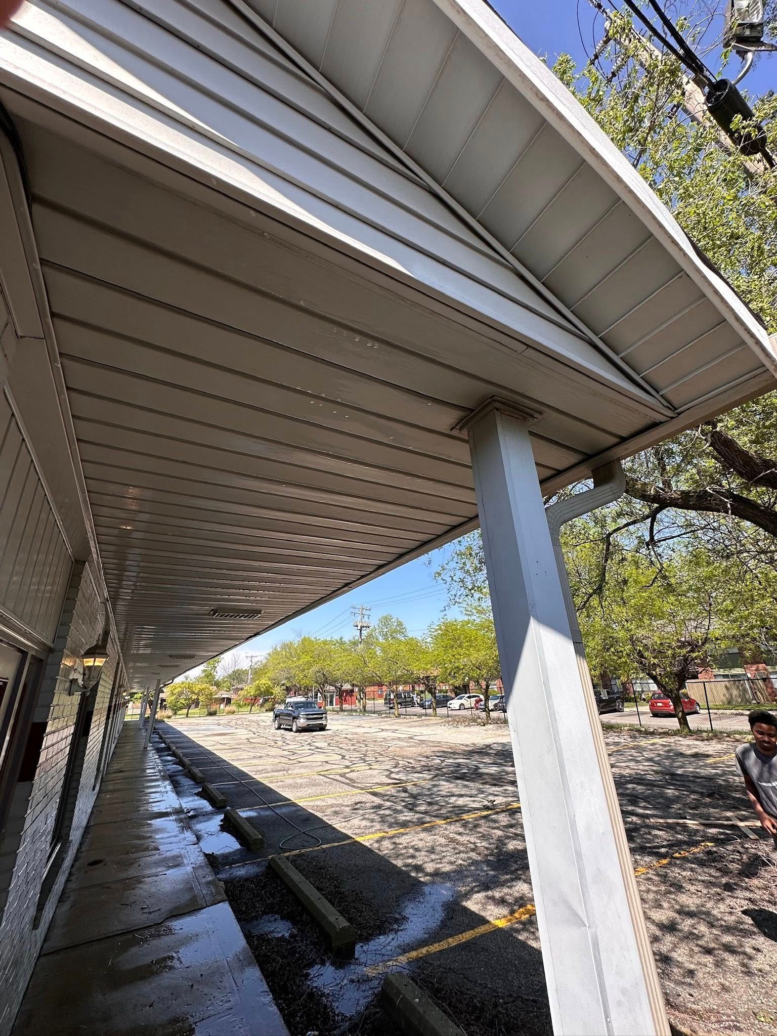 Covered walkway beside a wet parking lot with trees and cars under a clear blue sky
