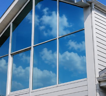 Large house window reflecting a blue sky with clouds, framed by white siding and trim