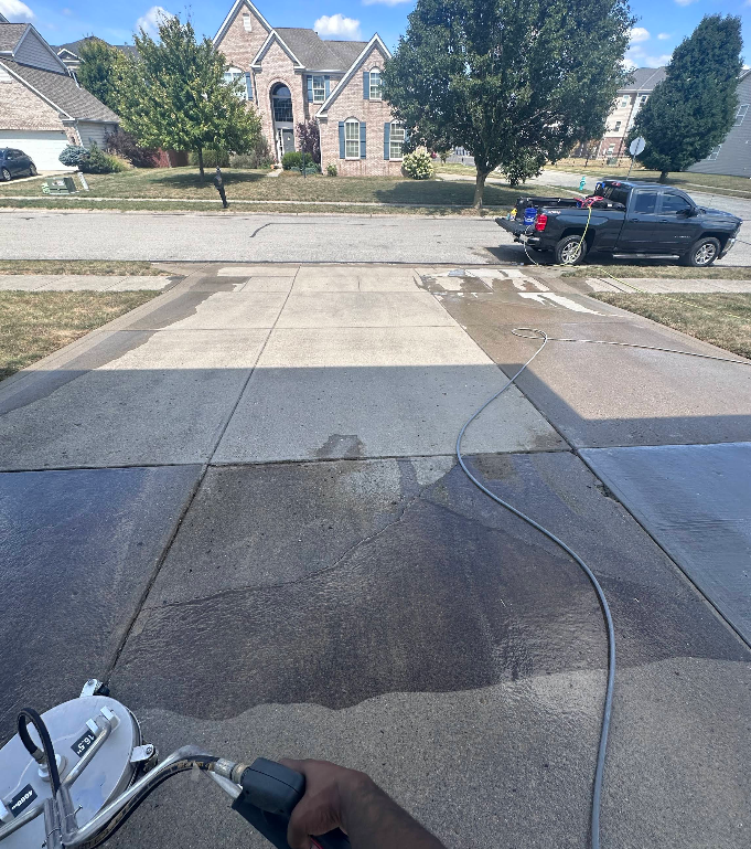 Driveway view with a black pickup on the street, a hose across the pavement, and houses in the background.