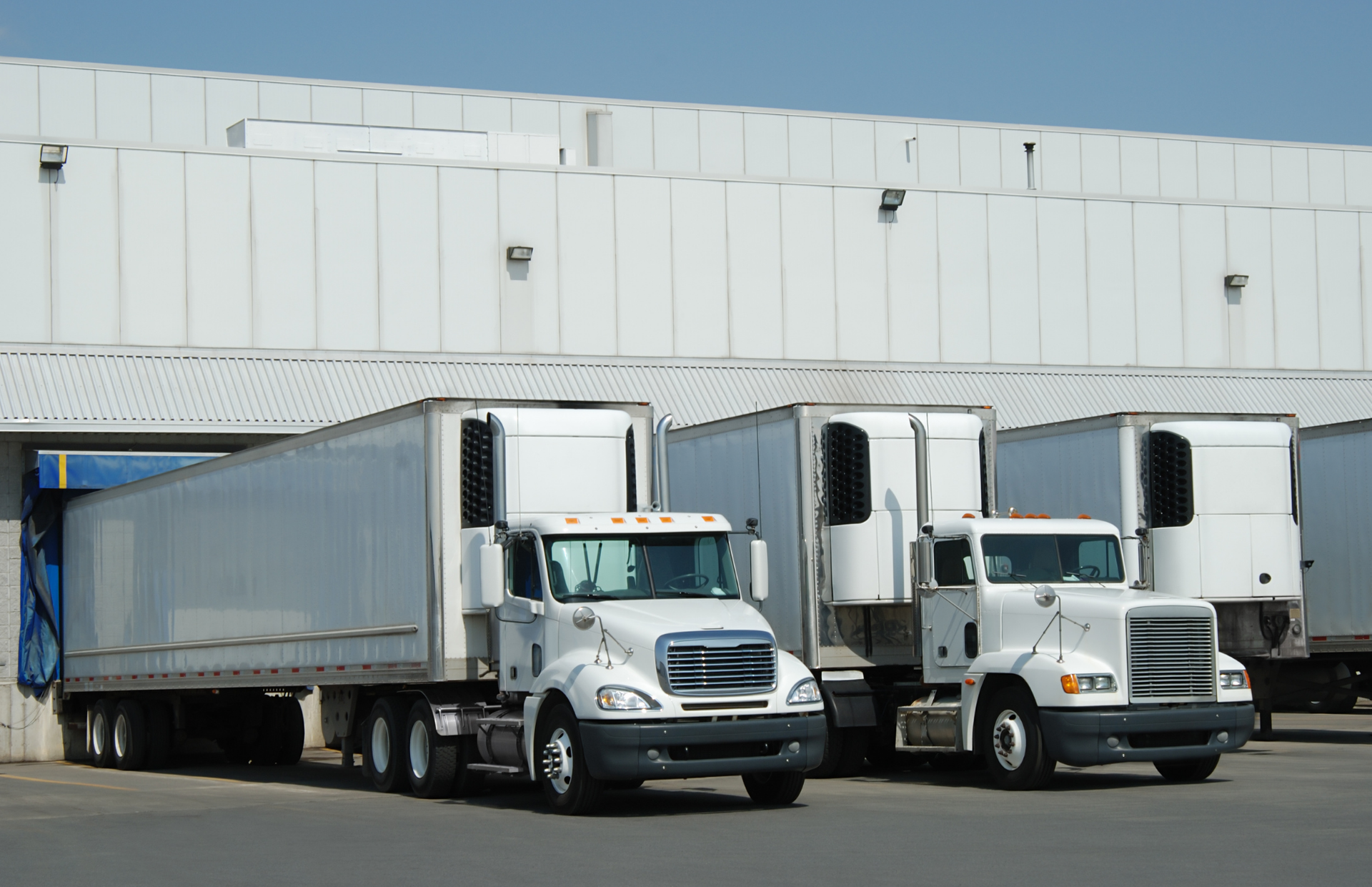 Three white delivery trucks parked in front of a warehouse loading dock.