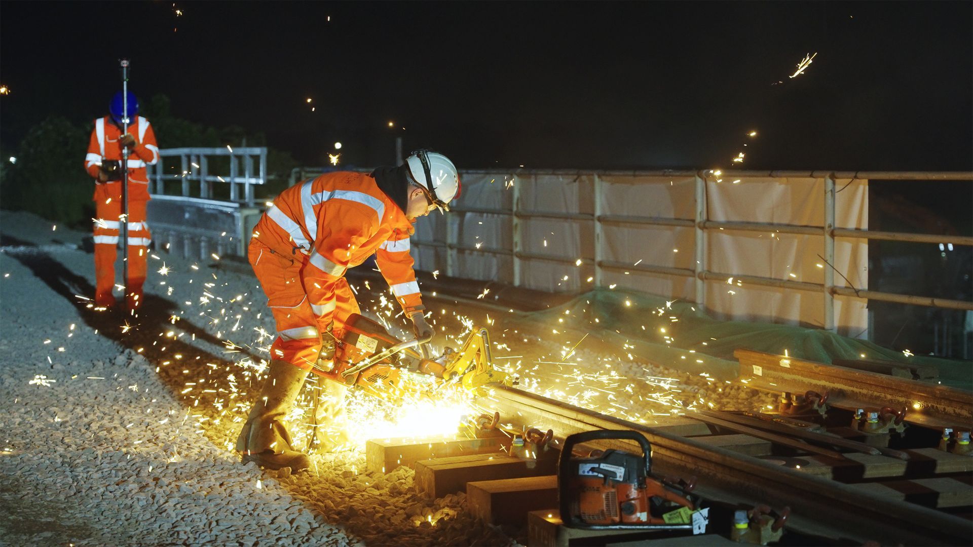 a man is cutting a piece of metal on a train track at night .