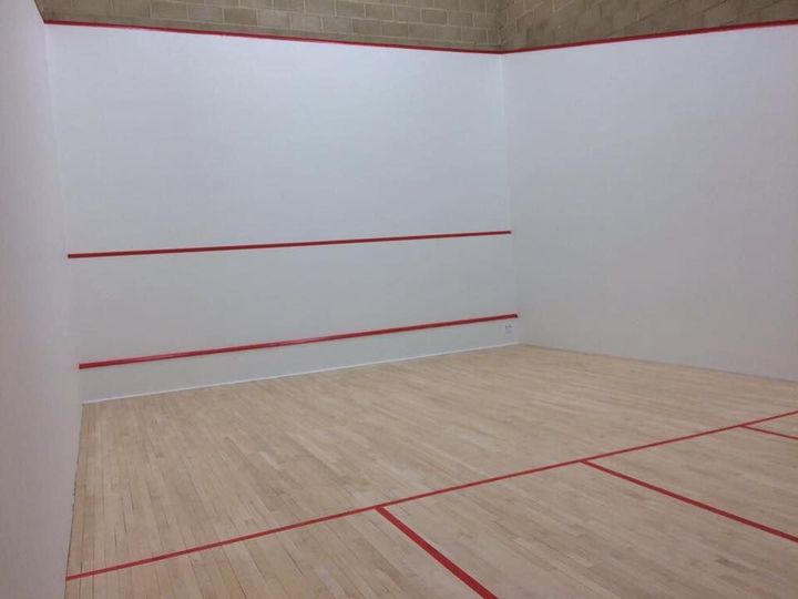 A squash court with a wooden floor and white walls.
