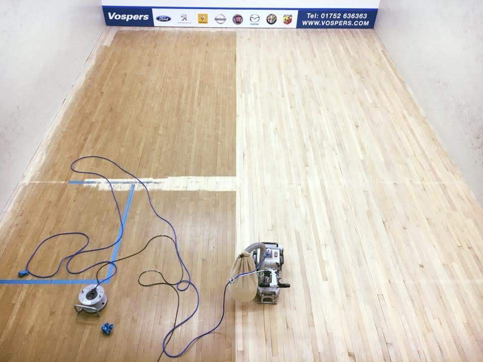 A wooden squash floor is being restored in a squash court.