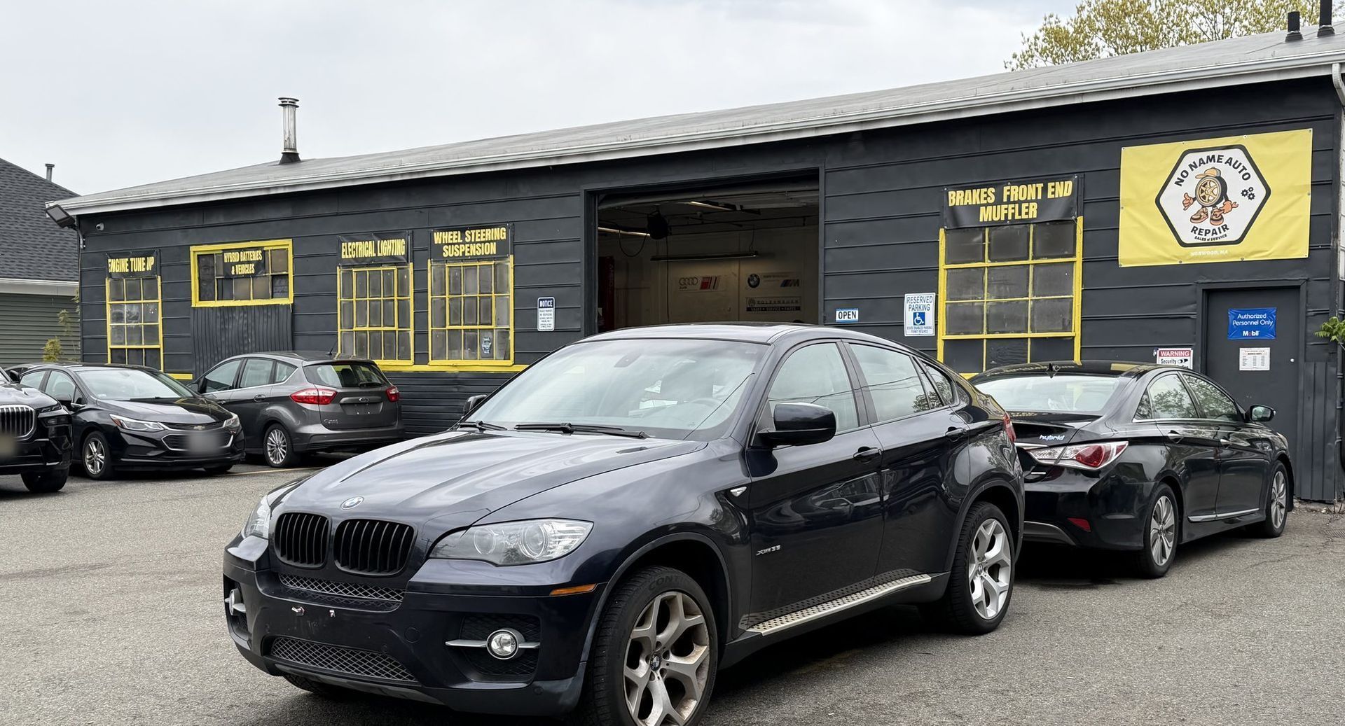 No Name Auto Repair at 64 Broadway, Norwood: the black building with yellow-framed windows, hand-painted service signs and the open service bay