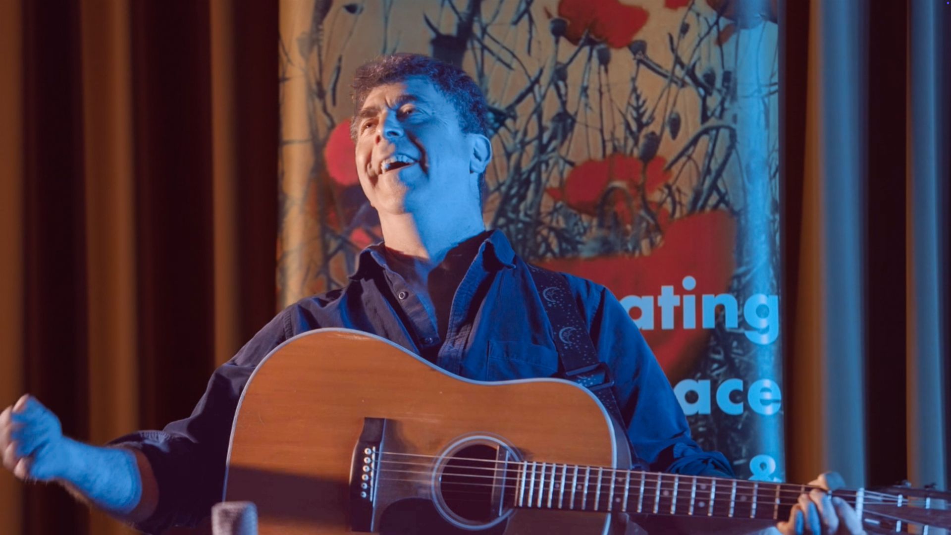 A man is playing an acoustic guitar in front of a curtain.