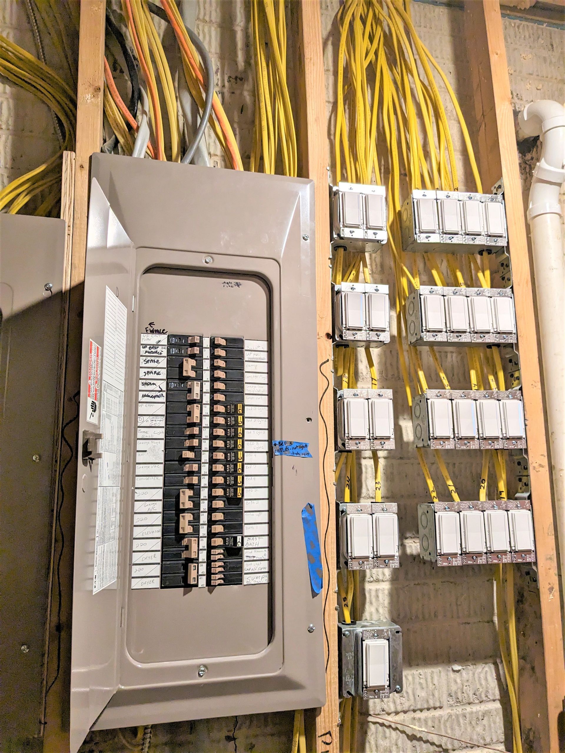 Open electrical breaker panel with rows of yellow and black wires in a utility room