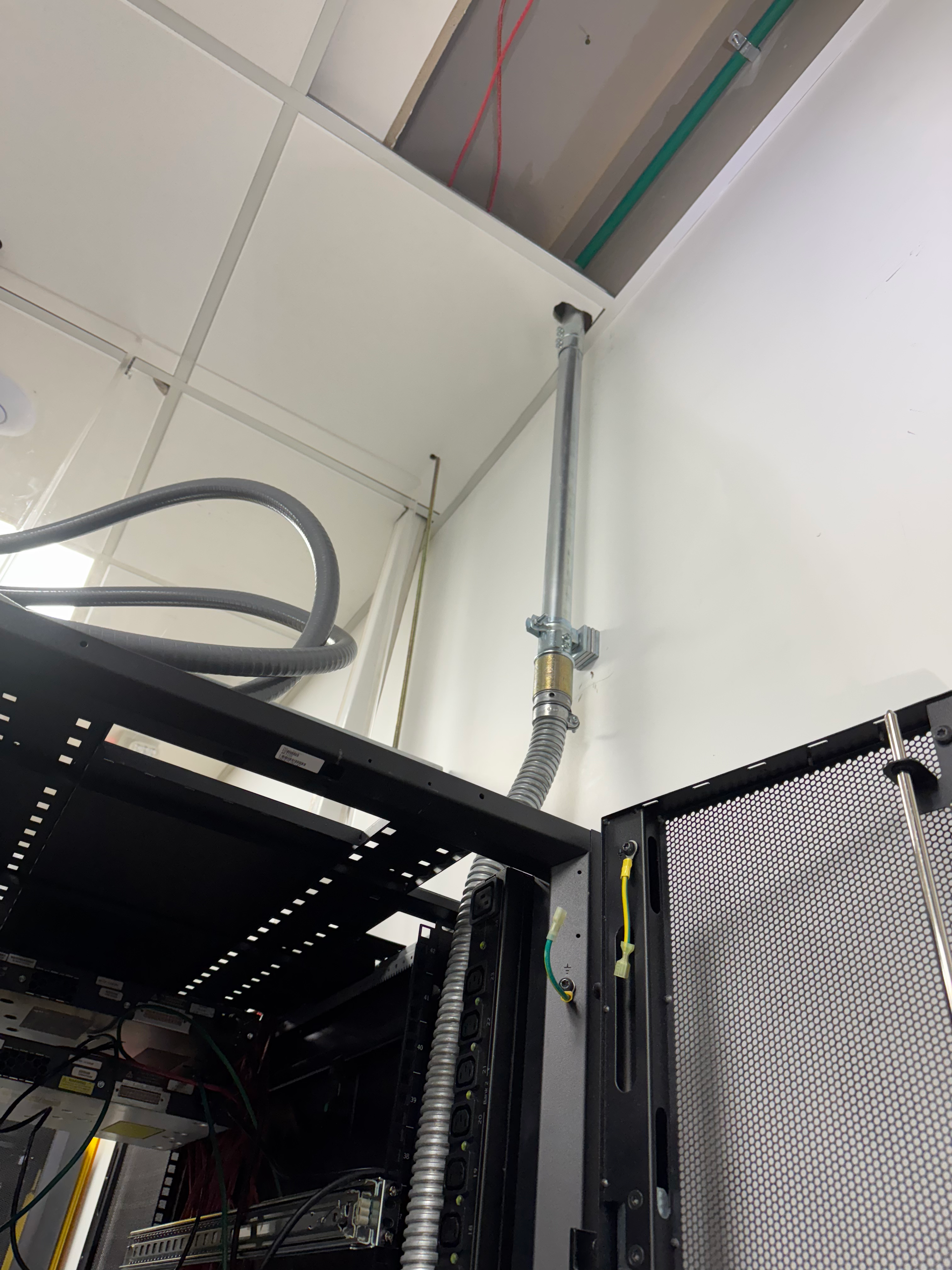 Ceiling-mounted pipes above black server racks in an industrial equipment room