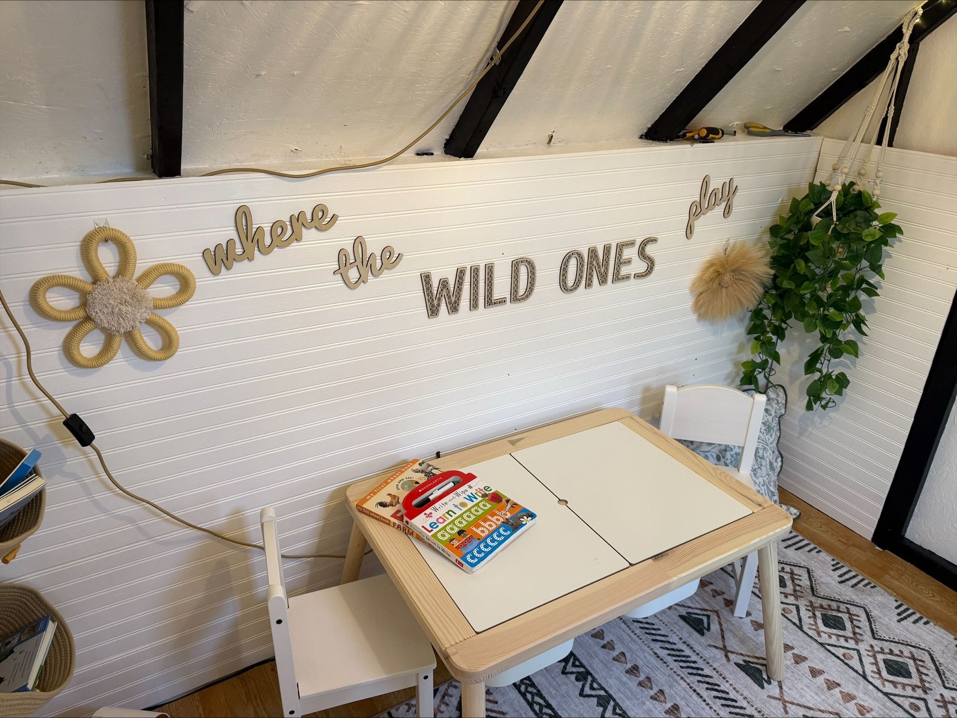 Cozy kids’ art nook with small table, chairs, wall decor, and string lights under a sloped ceiling