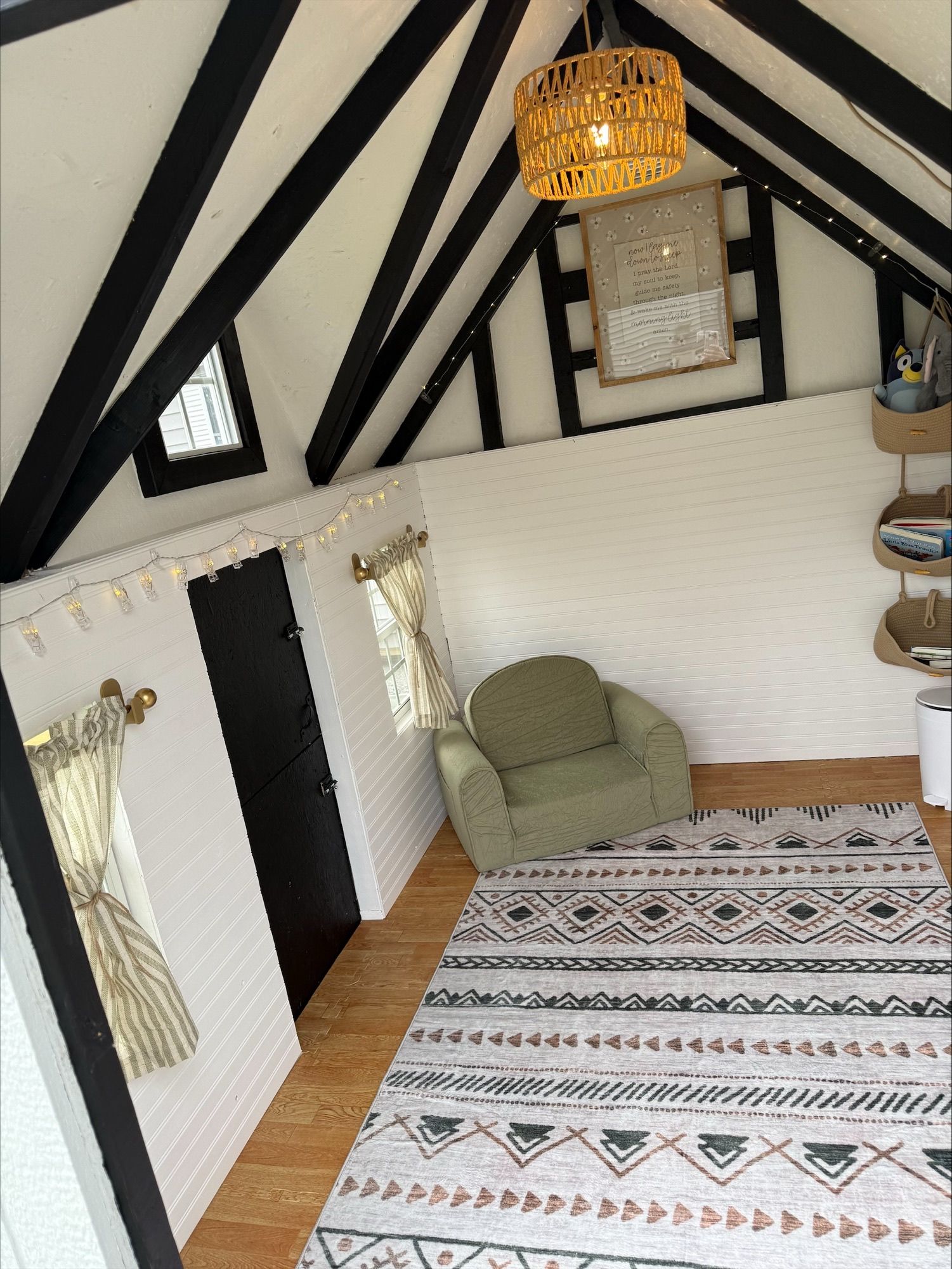 Cozy loft bedroom with black beams, green chair, patterned rug, and hanging wicker light.