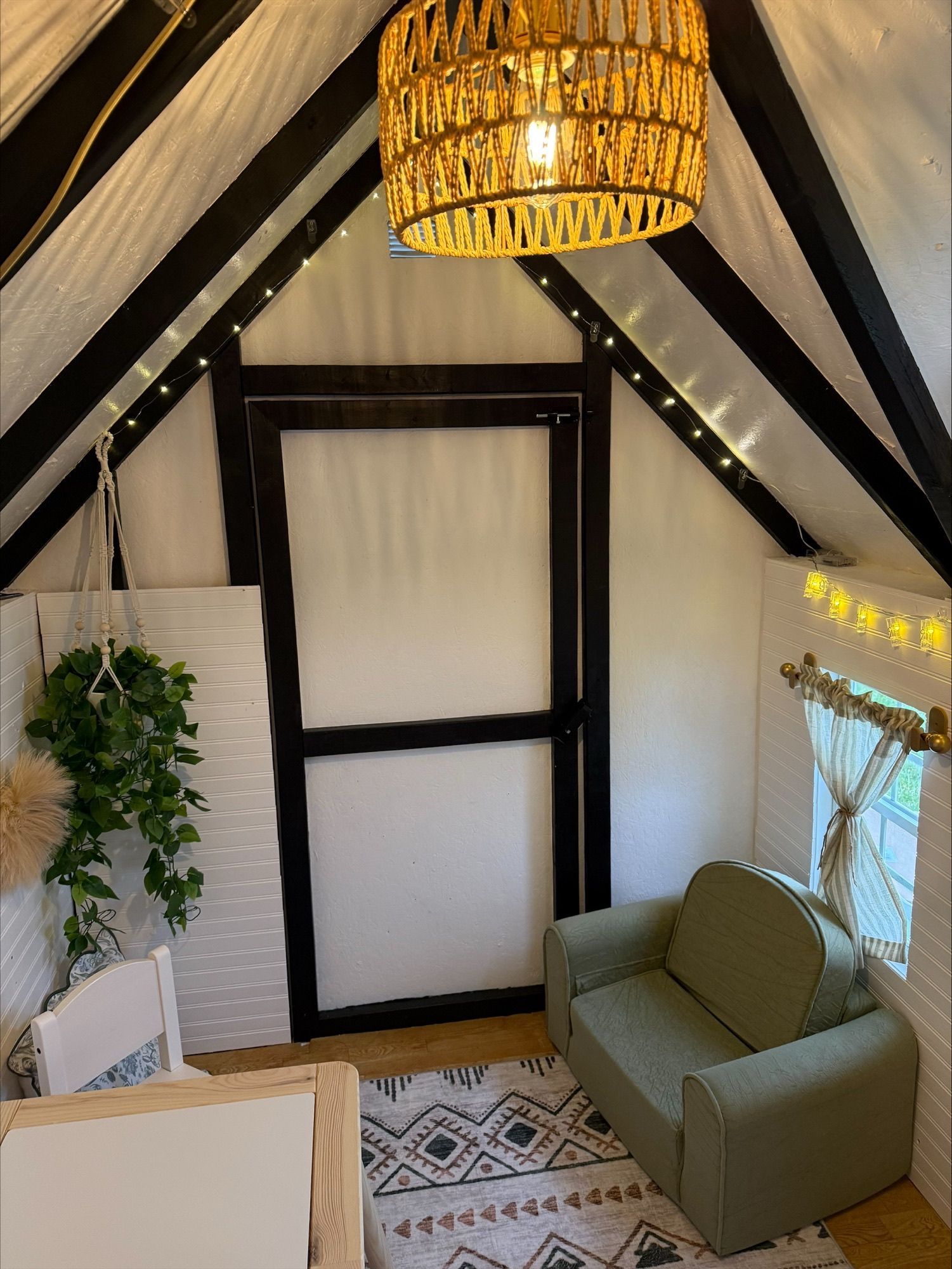 Cozy attic-style room with black beams, wicker pendant light, and a small green sofa by a window