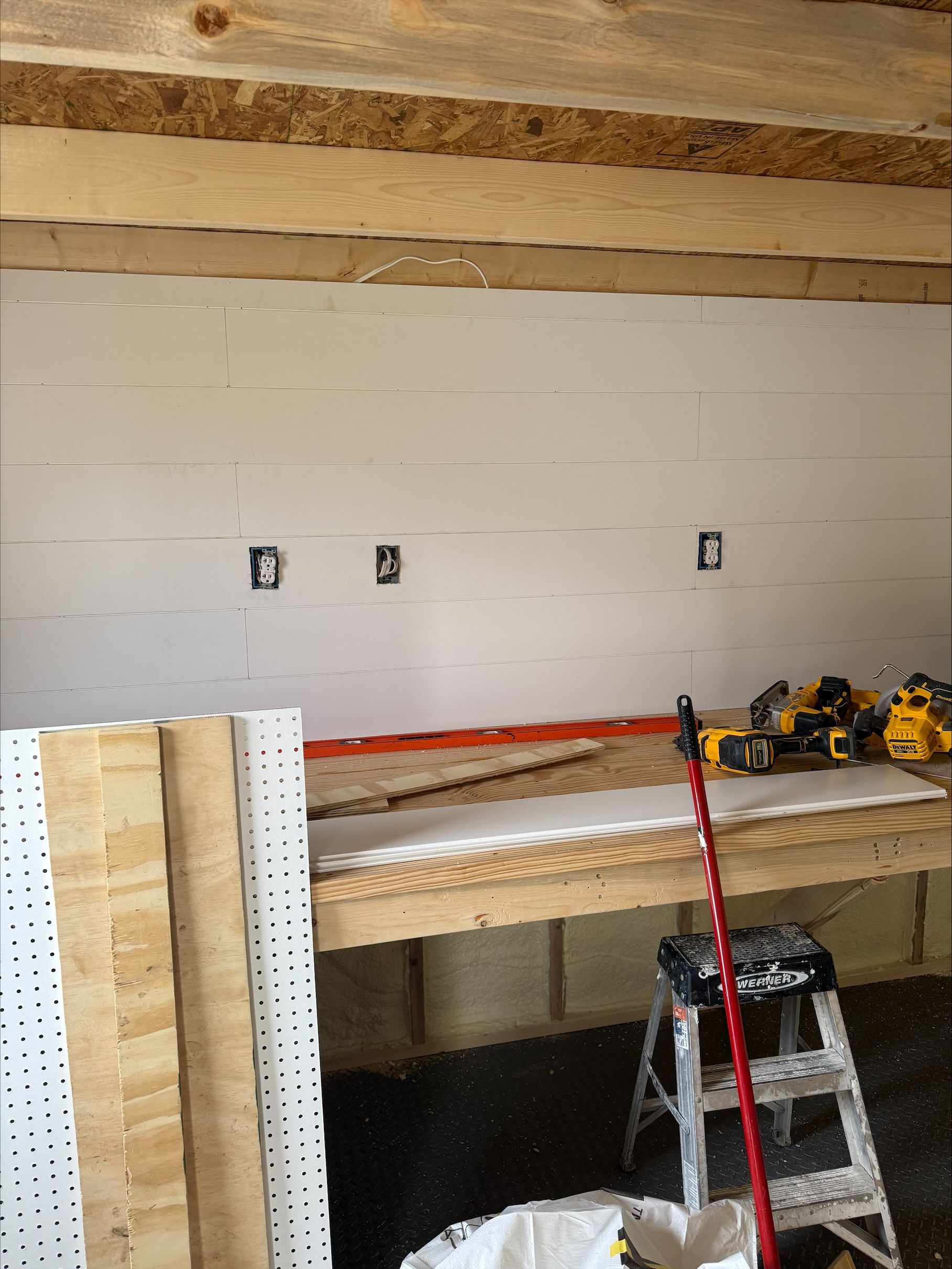 Construction workspace with unfinished wall, workbench, ladder, and tools in a garage-like room