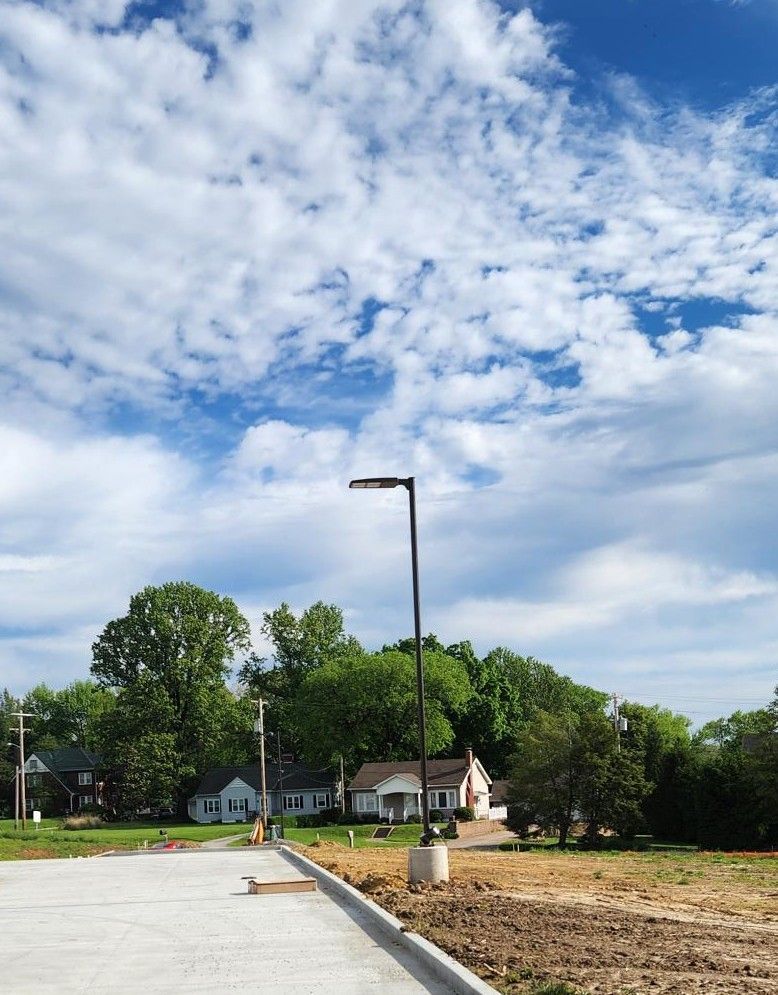 New residential street under a cloudy blue sky, with trees, houses, and a streetlight