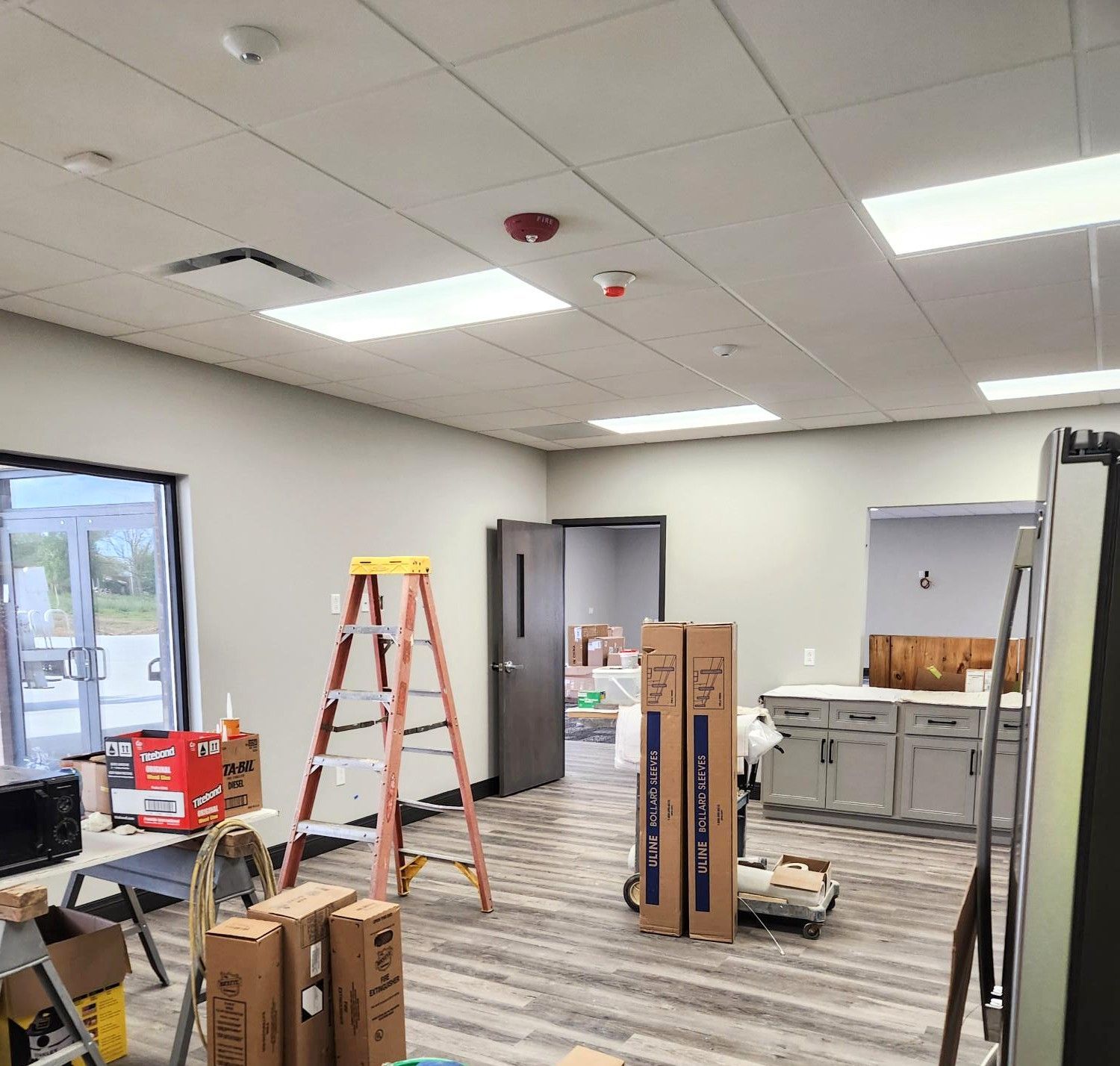 Office under renovation with ladders, boxes, and construction materials scattered across the floor.