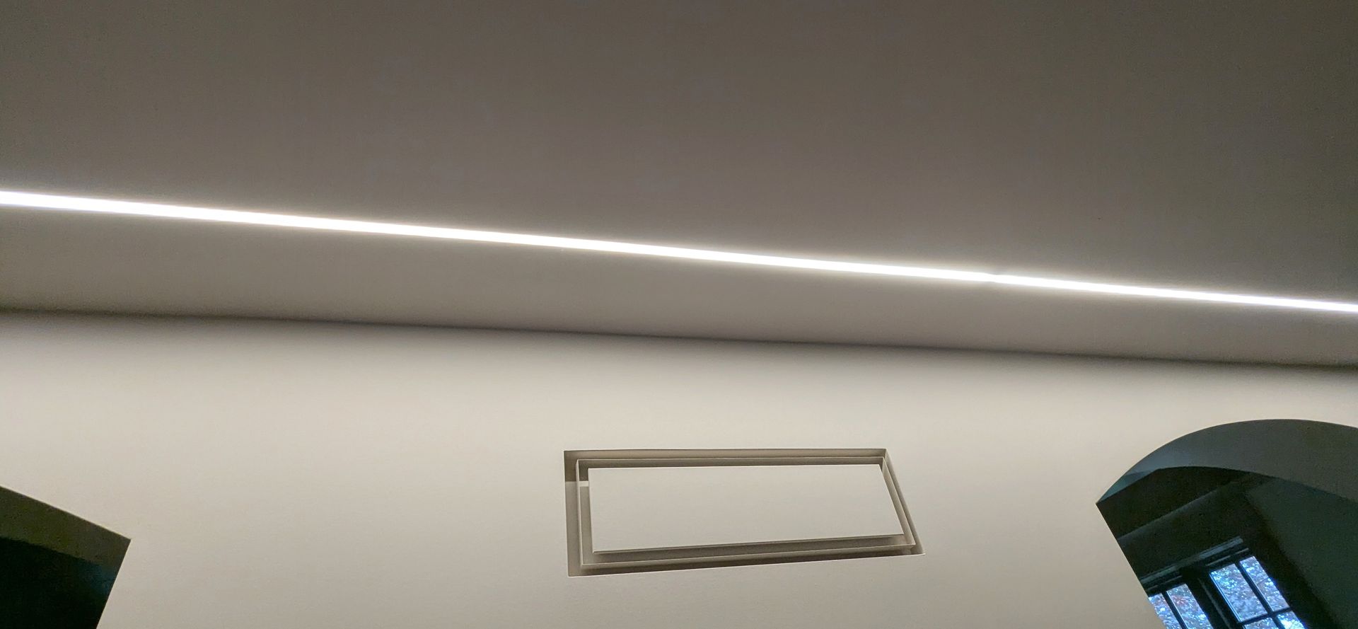 White wall with a small rectangular picture frame beneath a ceiling light strip.