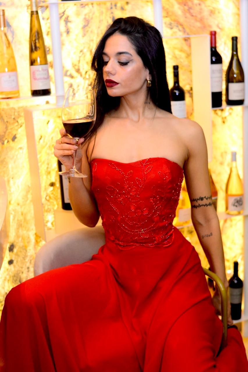 Una mujer con un vestido rojo sostiene una copa de vino.