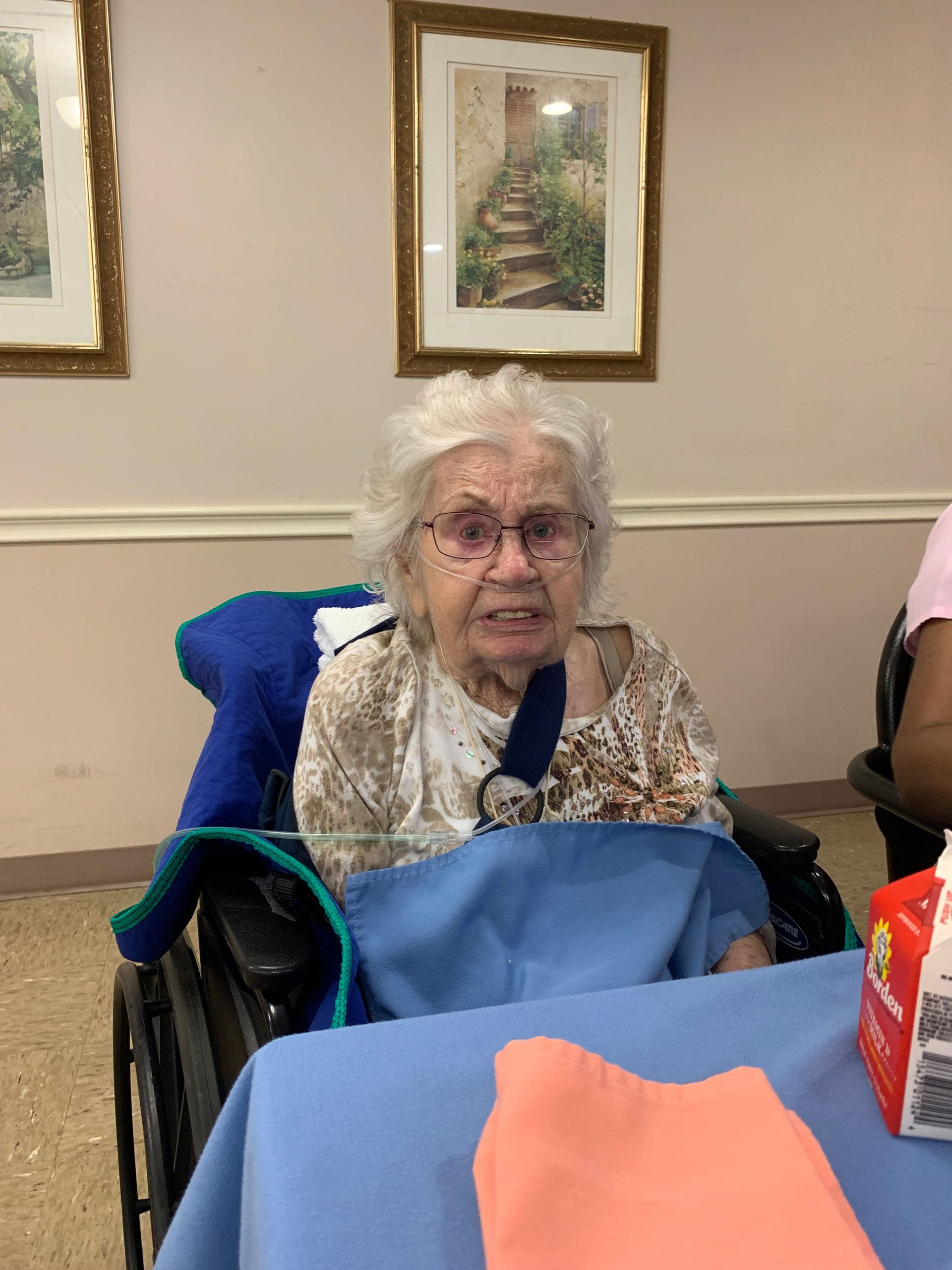 An elderly woman in a wheelchair is sitting at a table.