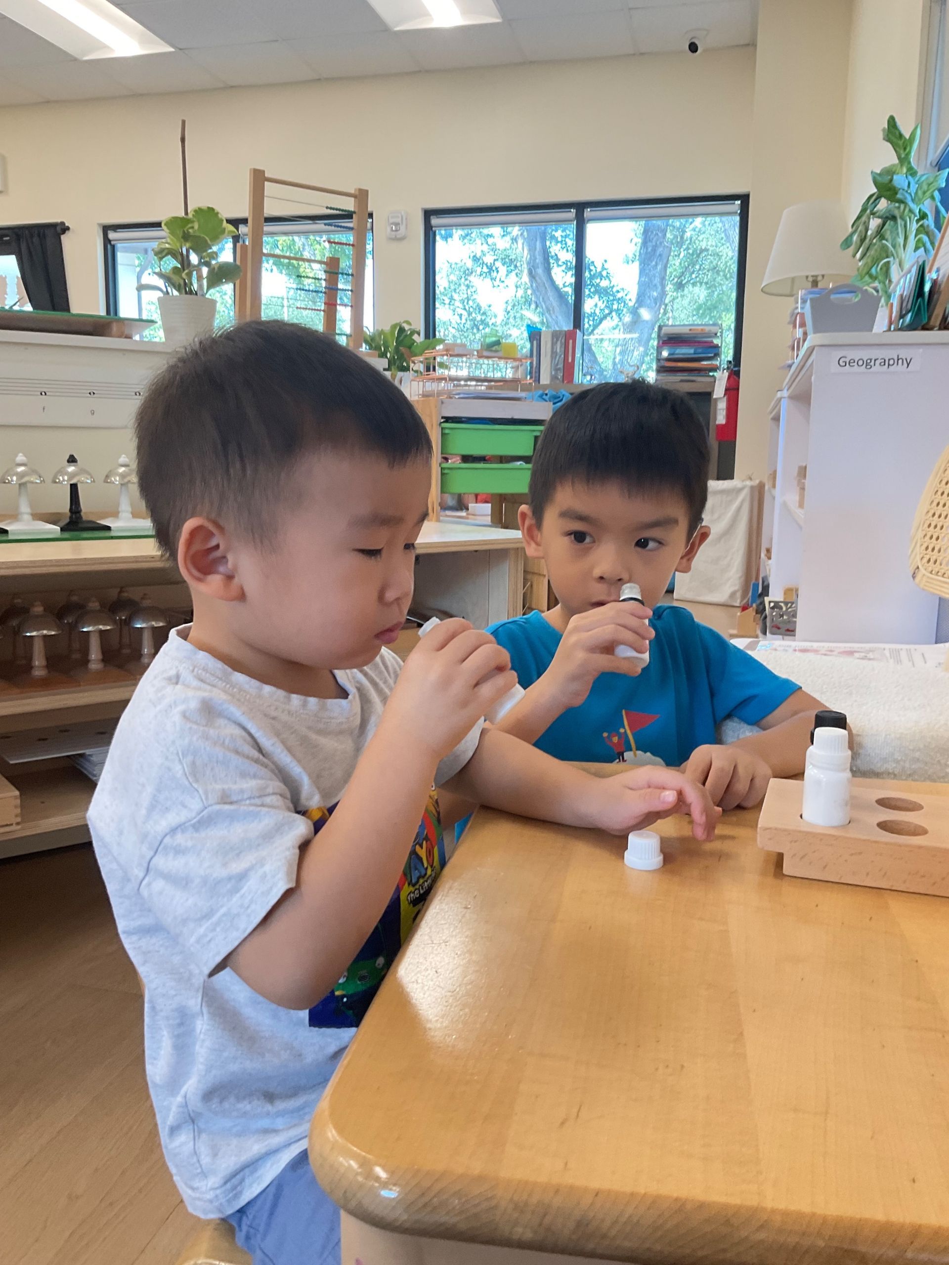 Two using the smelling bottles at a wooden table in a bright classroom