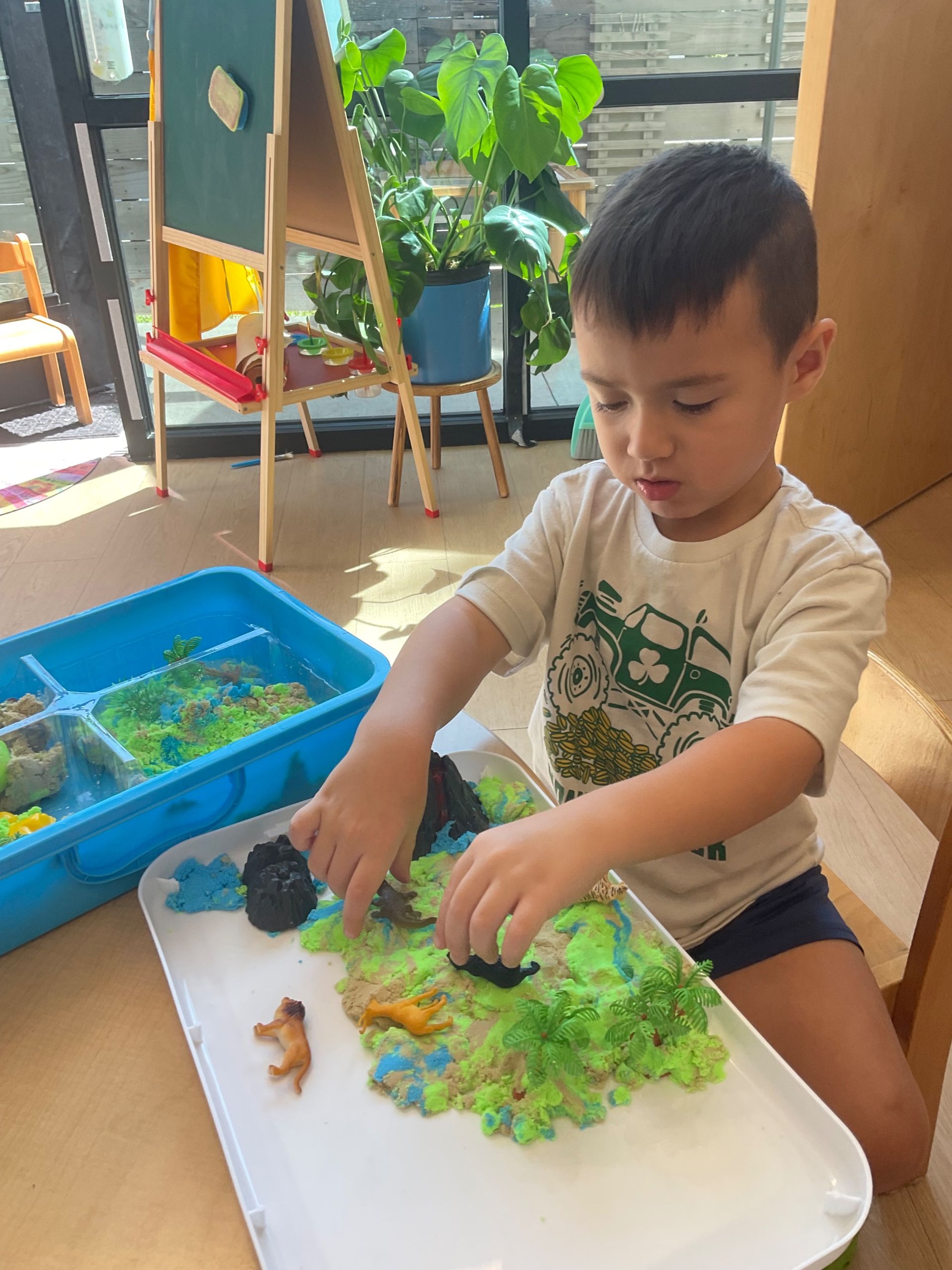 Child plays with colorful sensory materials at a table indoors.