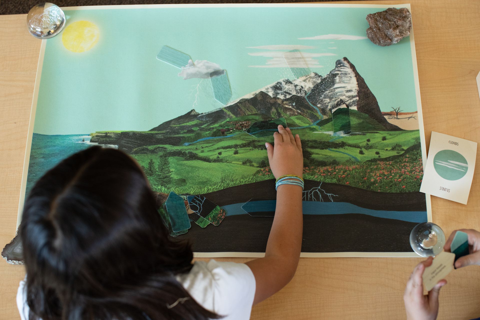 Person arranging a colorful mountain landscape collage on a board with glue and paper cutouts.