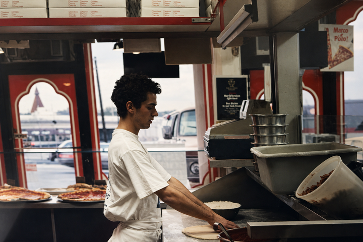 Worker in a white shirt cooking behind a counter in a restaurant kitchen.