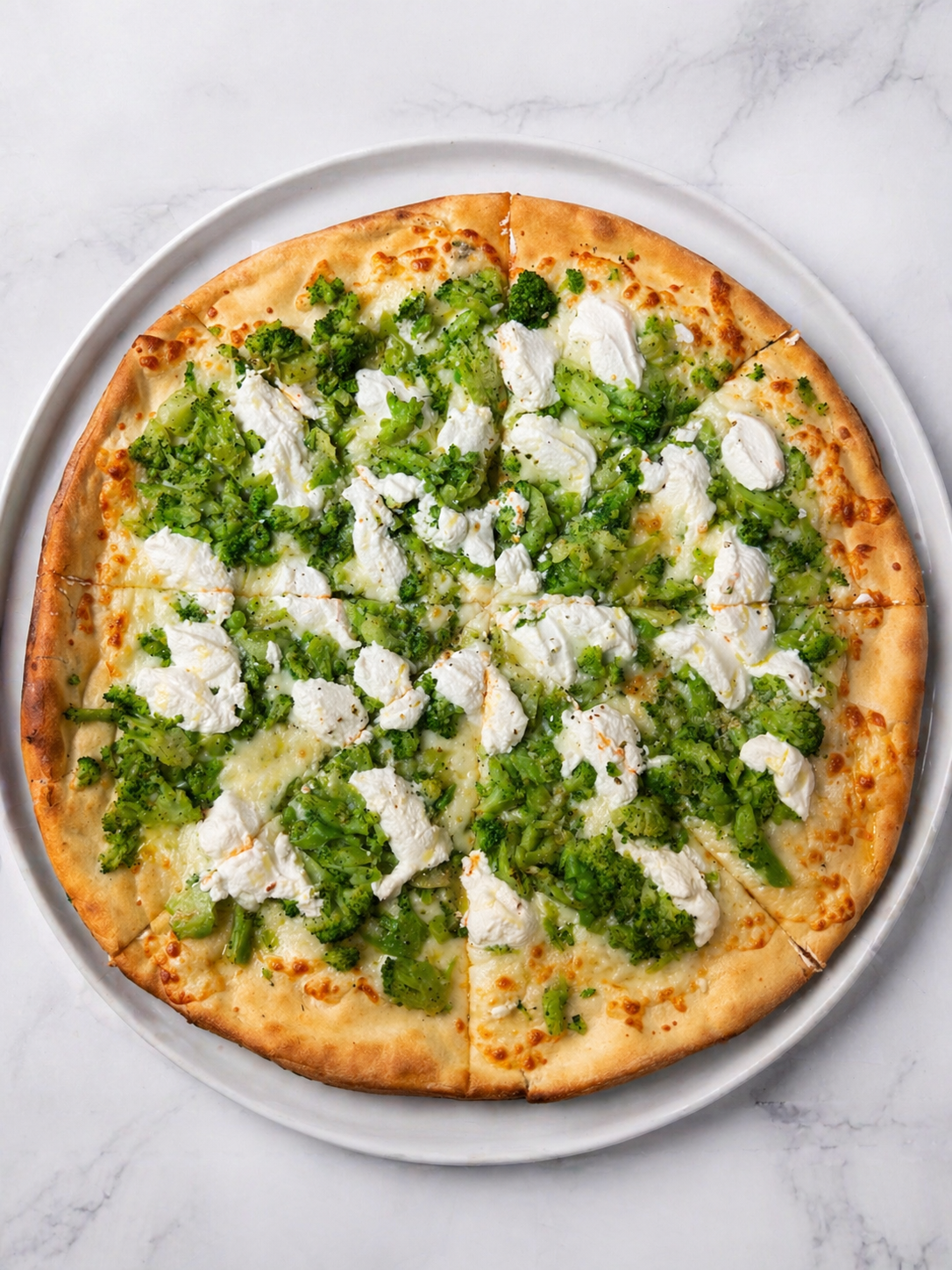 White pizza topped with green broccoli and dollops of ricotta on a plate.