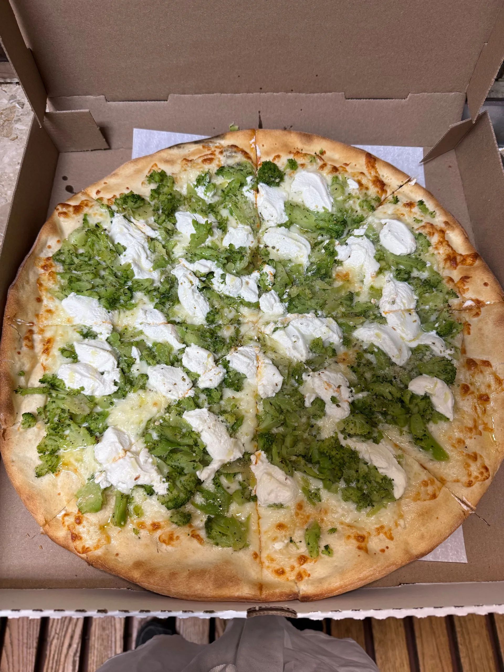 Open pizza box with a green pesto and white cheese pizza