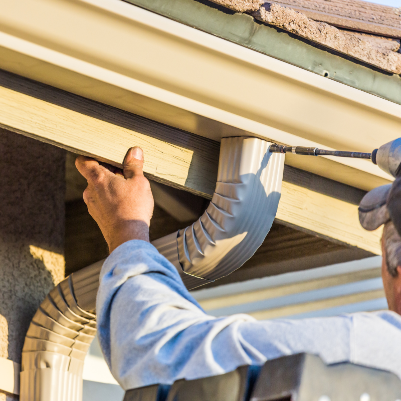 A man is using a drill to fix a gutter on a house