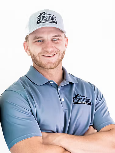 A man wearing a hat and a blue polo shirt is standing with his arms crossed.
