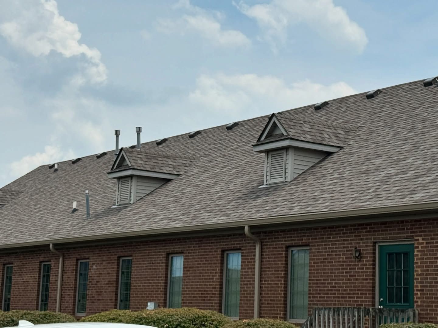 A brick building with a gray roof and a green door