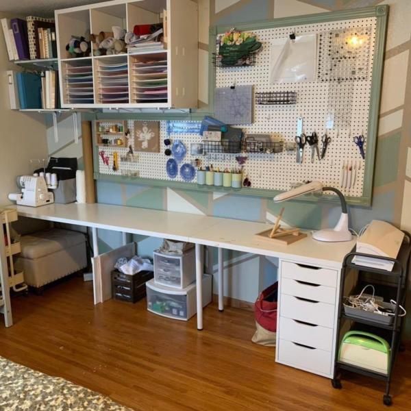 Craft room with white desk and storage, pegboard, sewing machine, and rolling cart.