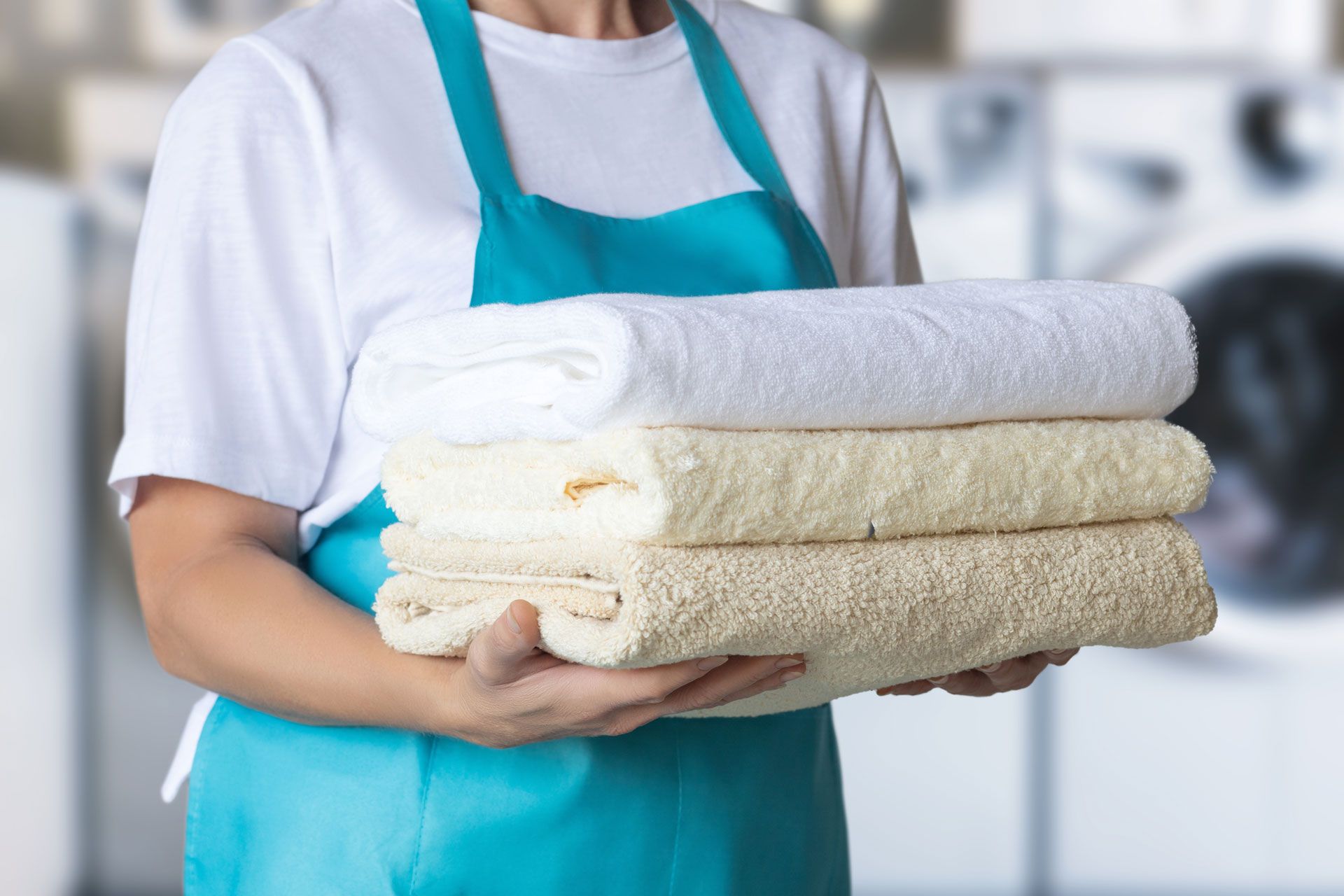 Person holding a stack of folded white and beige towels in a laundromat setting.