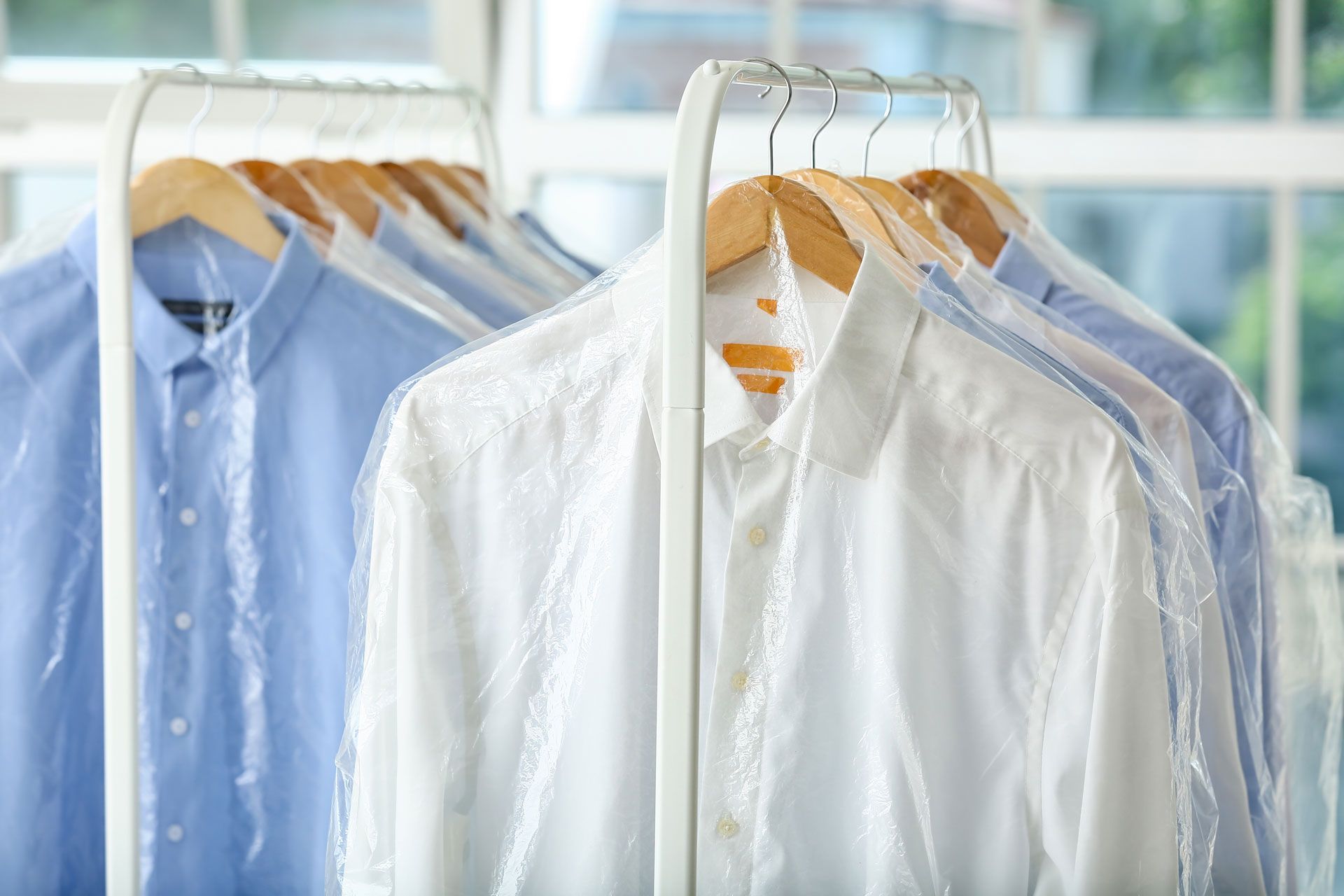 Shirts on hangers covered with plastic at a dry cleaner's, white and blue.
