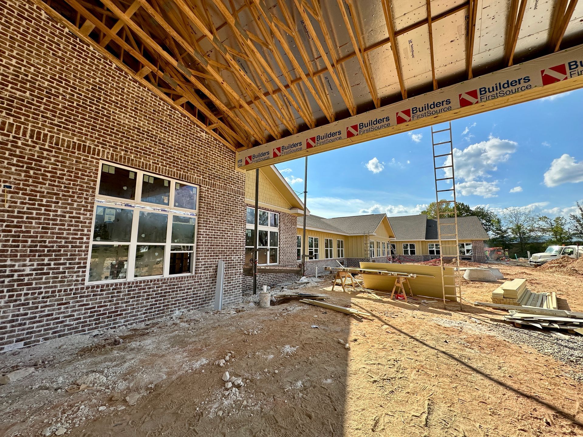 Construction site: brick building exterior with exposed wood framing, windows, and materials. Blue sky.