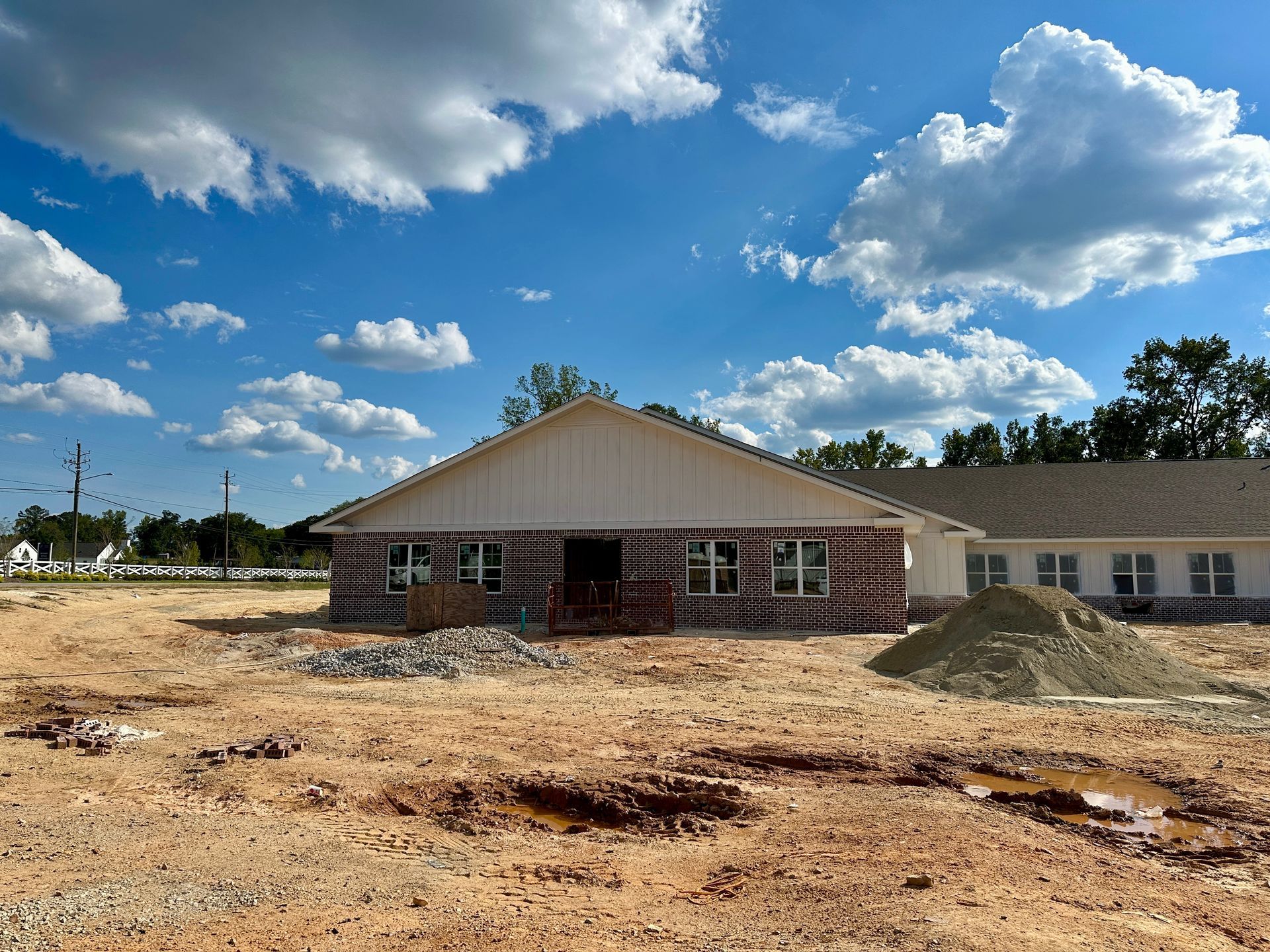 Construction site, building frame with white siding, brown dirt ground, blue sky with clouds.