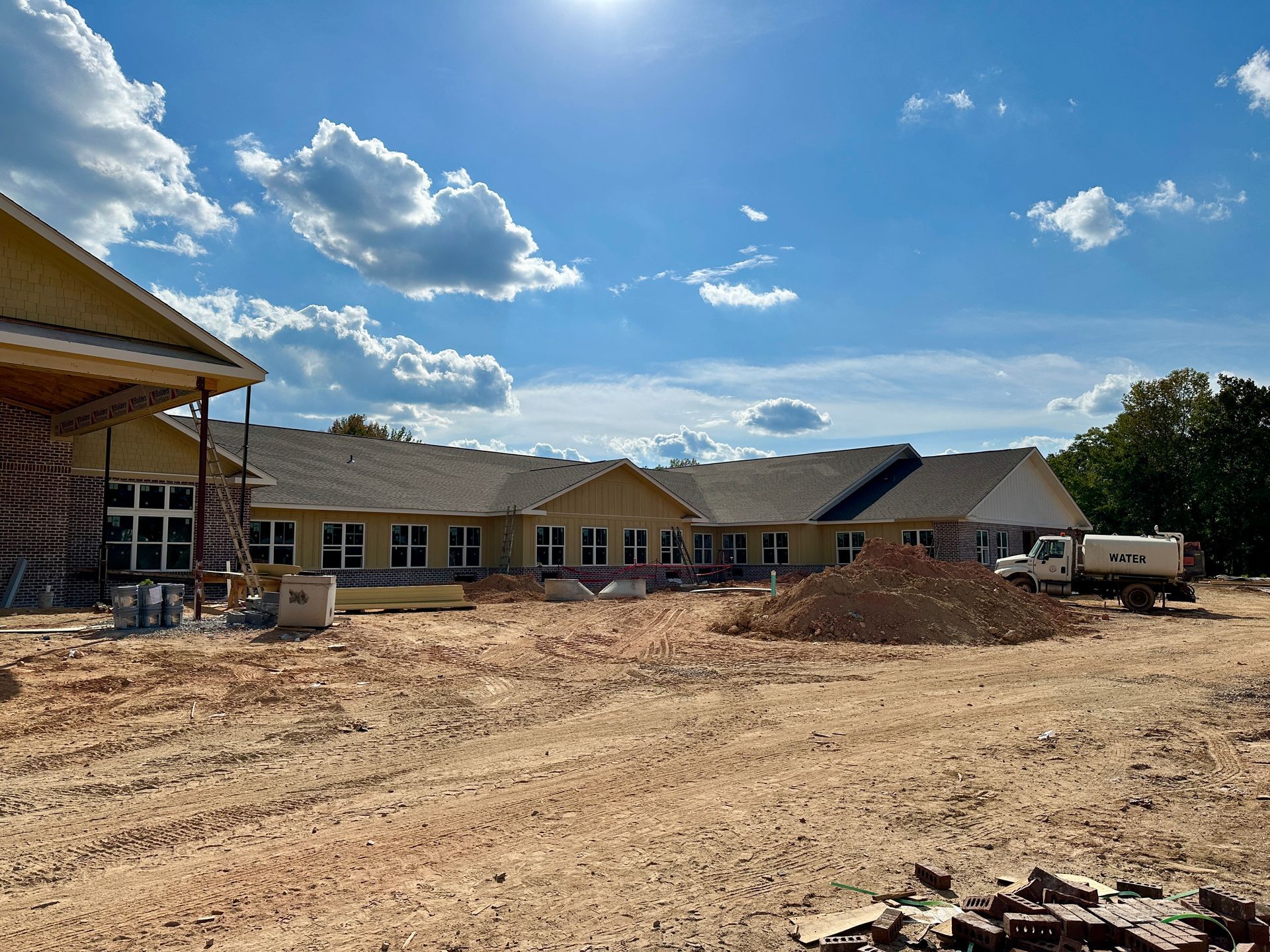 Construction site: One-story building under construction with dirt lot. Blue sky with white clouds overhead.