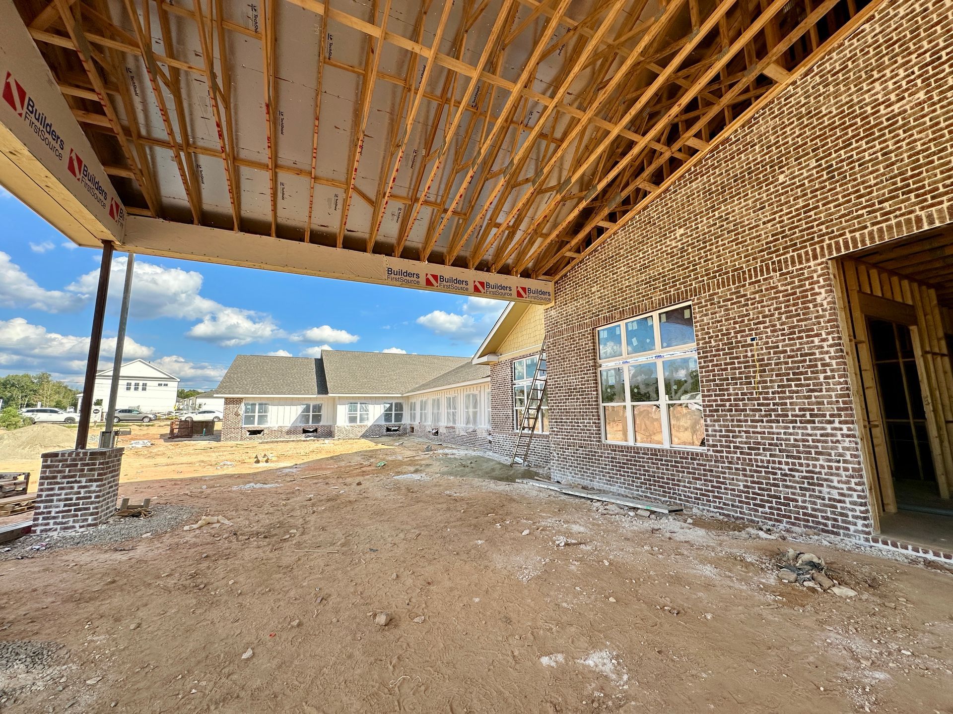 Construction site, brick house exterior with exposed rafters. Cloudy sky.
